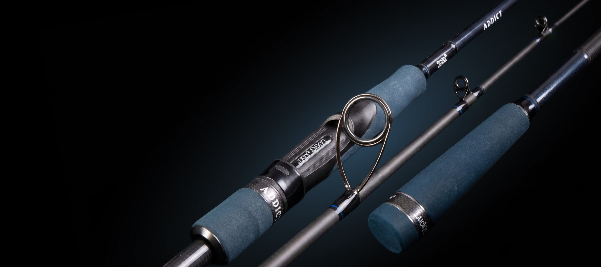 A close-up studio shot of a fishing rod with blue-green wrapped grips and a dark metallic blank, shown against a black background. The rod is positioned diagonally with another section visible behind it.