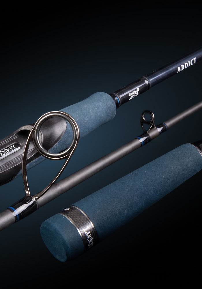 A close-up studio shot of a fishing rod with blue-green wrapped grips and a dark metallic blank, shown against a black background. The rod is positioned diagonally with another section visible behind it.