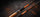 Two fishing rods with orange and black sections and light wood handles, arranged diagonally on a dark textured surface with scattered orange specks.