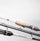 Close-up of fishing rods with white and black shafts, a light wood handle grip, and metallic reel seats on a plain light gray background.