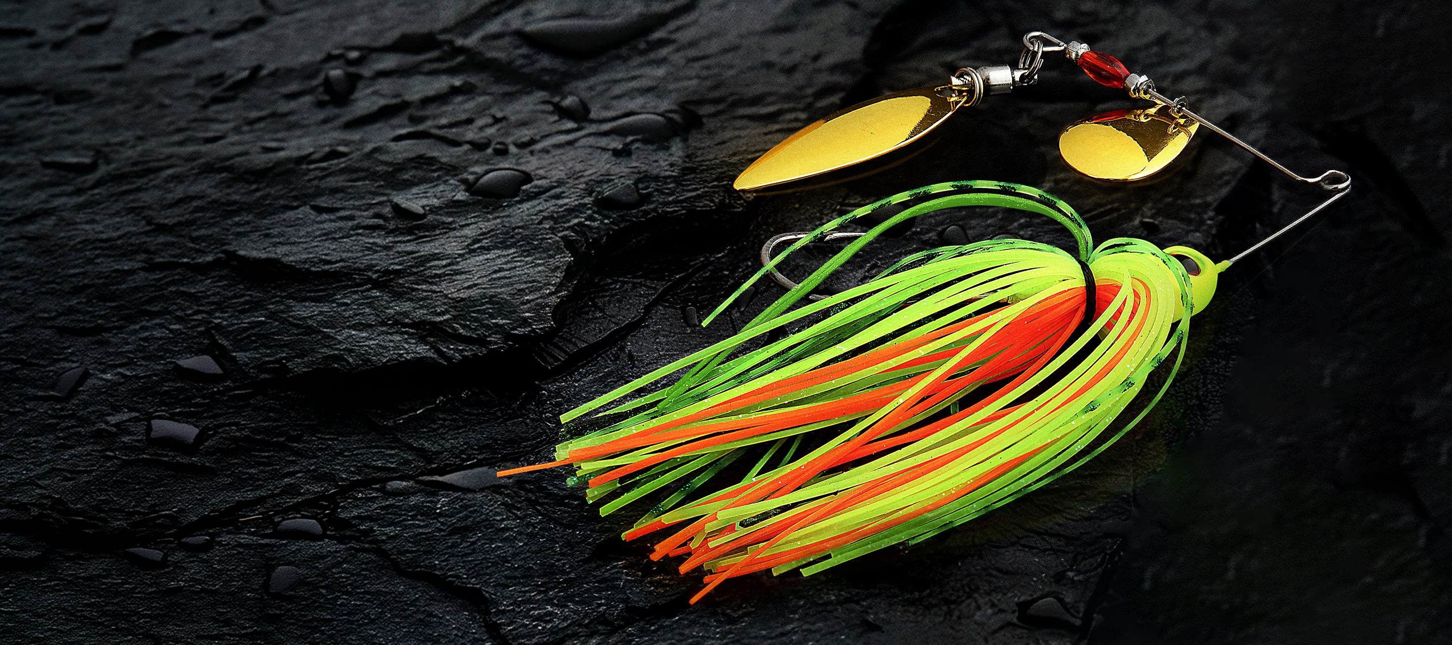 A fishing lure with a yellow spinner blade and a skirt made of neon green, orange, and yellow strands, photographed on a dark textured surface.