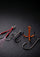 Four fishing hooks arranged on a dark textured surface, including two silver treble hooks with red and pink line wraps and two orange treble hooks.