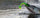 A bright green and yellow soft plastic fishing lure is being bitten by a large fish jumping out of the water, with ripples on the surface and a blurred natural background.