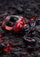 A red and black baitcasting fishing reel with a black handle, resting on a dark textured surface with glowing red embers.